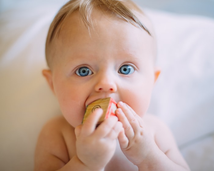 A wide-eyed infant exploring a smooth wooden block with their hands