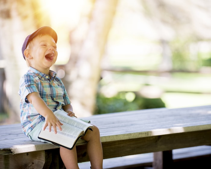A delighted Pre-K child laughing with an open picture book outdoors