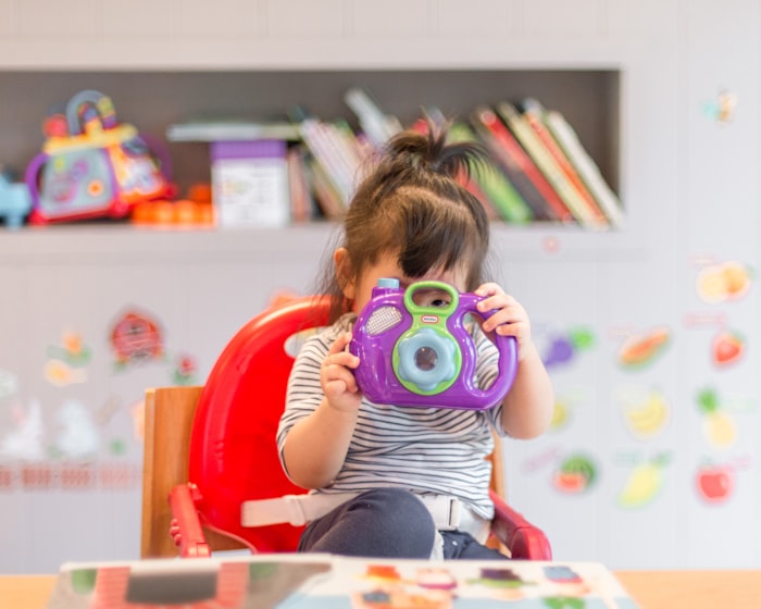 A happy toddler playing with a colorful toy camera in a bright, decorated playroom