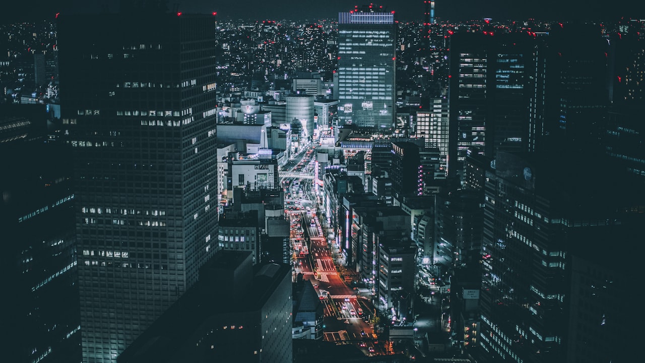 An aerial view of a vast neon-lit city at night, threaded with glowing traffic.