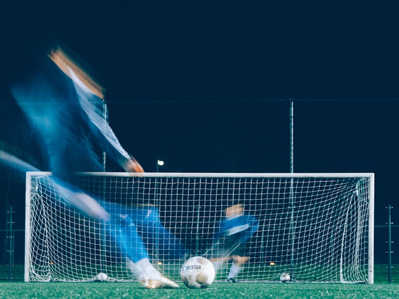 A player striking the ball into the net under the floodlights at night