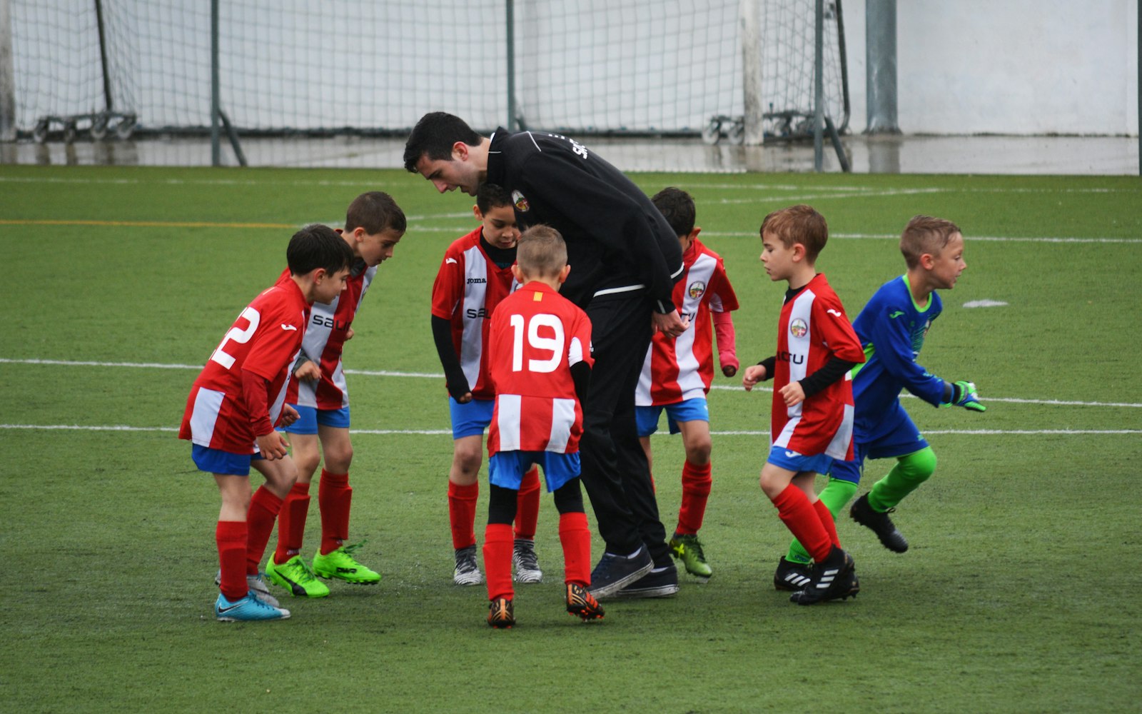 A youth football coach gathering a team of young players in red kit on the training pitch