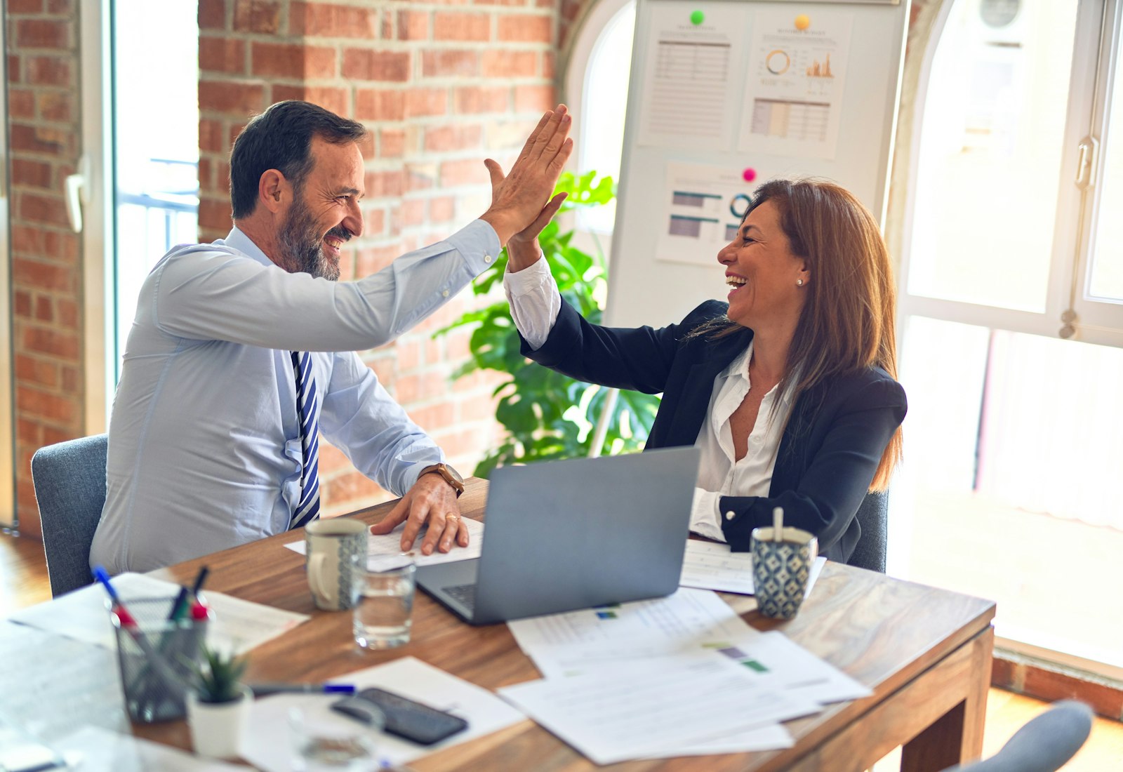 A recruiter and a hiring manager celebrating a successful placement with a high five across an office desk