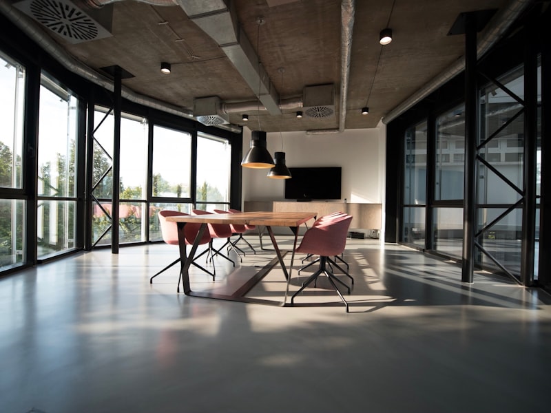 Private glass-walled office room with a wooden table and soft chairs, lit by floor-to-ceiling windows