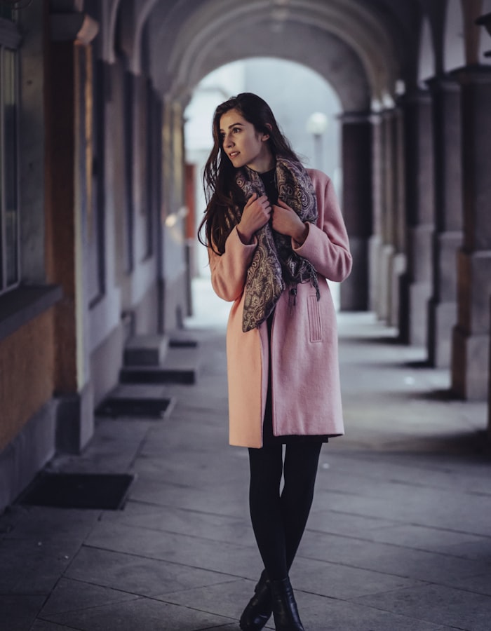 Model in a fluid blush wool wrap coat in a stone colonnade