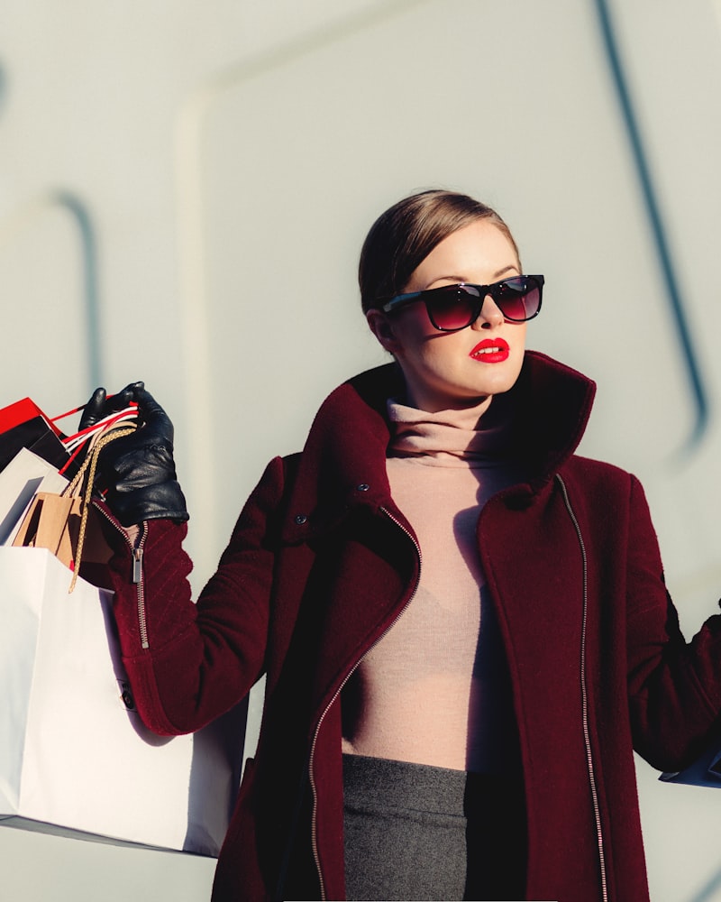 Model in a burgundy coat and sunglasses carrying a bag on a city street