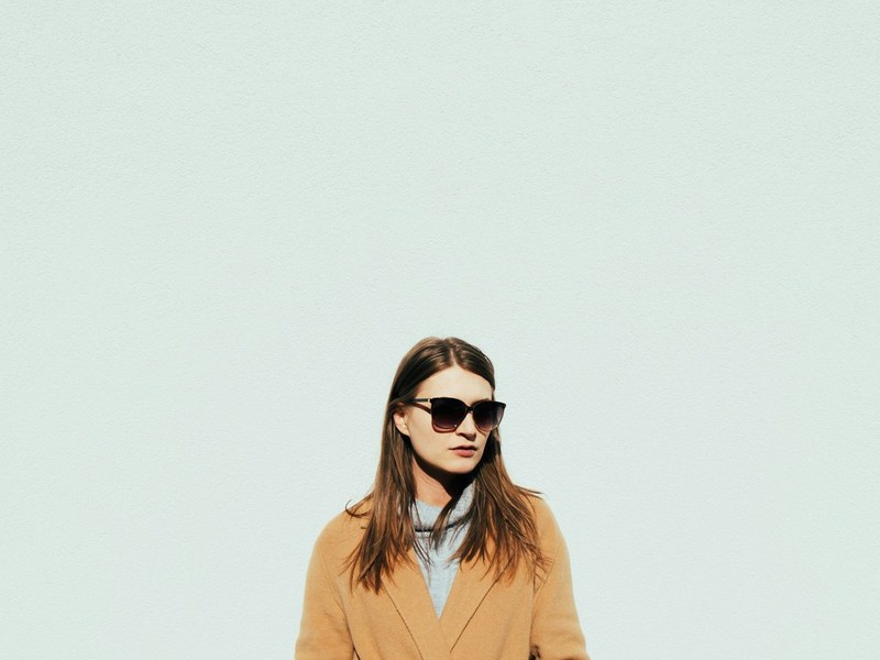 Model in a camel coat with gold accents, photographed in warm evening light
