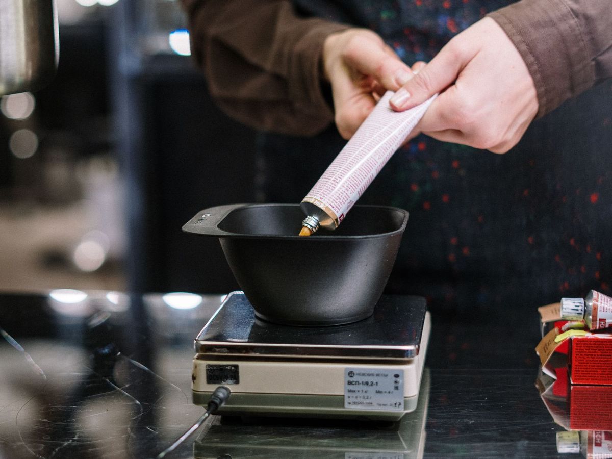 A colourist weighs and mixes hair dye in a bowl on a small scale