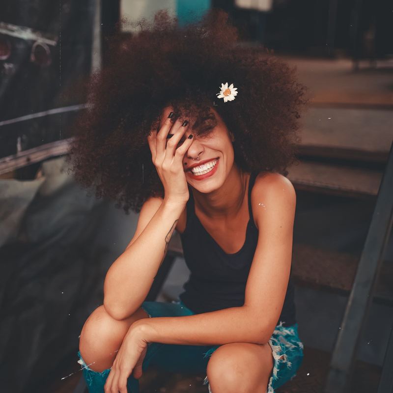 A client with glossy defined curls laughs towards the camera