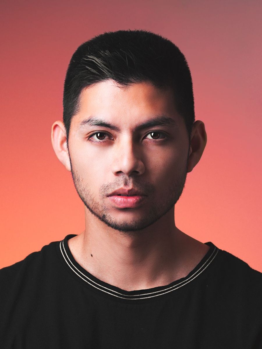 Marko, a stylist with a sharp dark crop, photographed against a warm backdrop