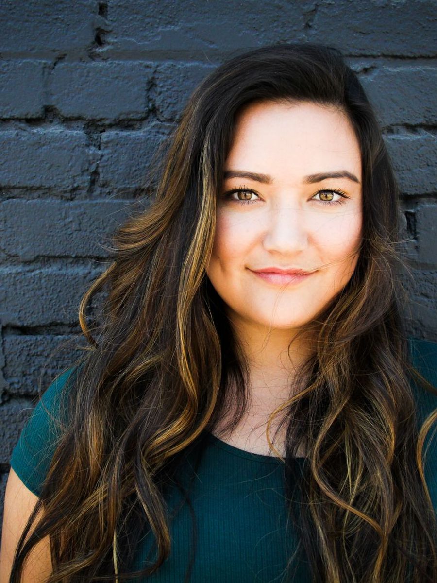 Nia with long dark waves photographed against a dark brick wall