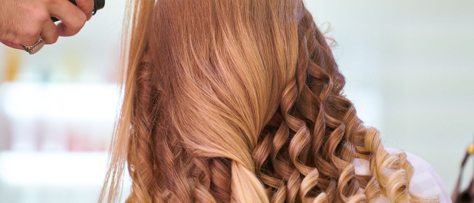 A curling iron forms a soft wave in blonde hair