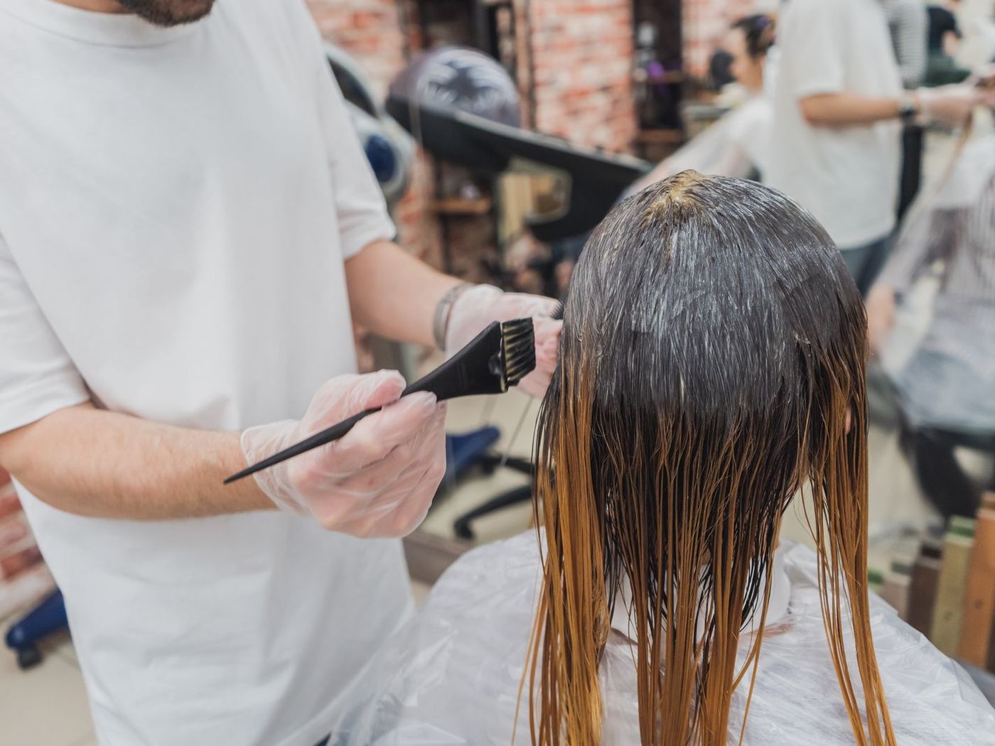 A colourist paints colour onto a client's hair in the bright studio