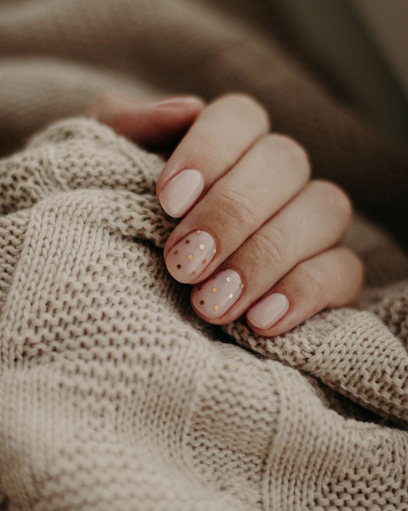 Milky nails with tiny dots against a knit sleeve
