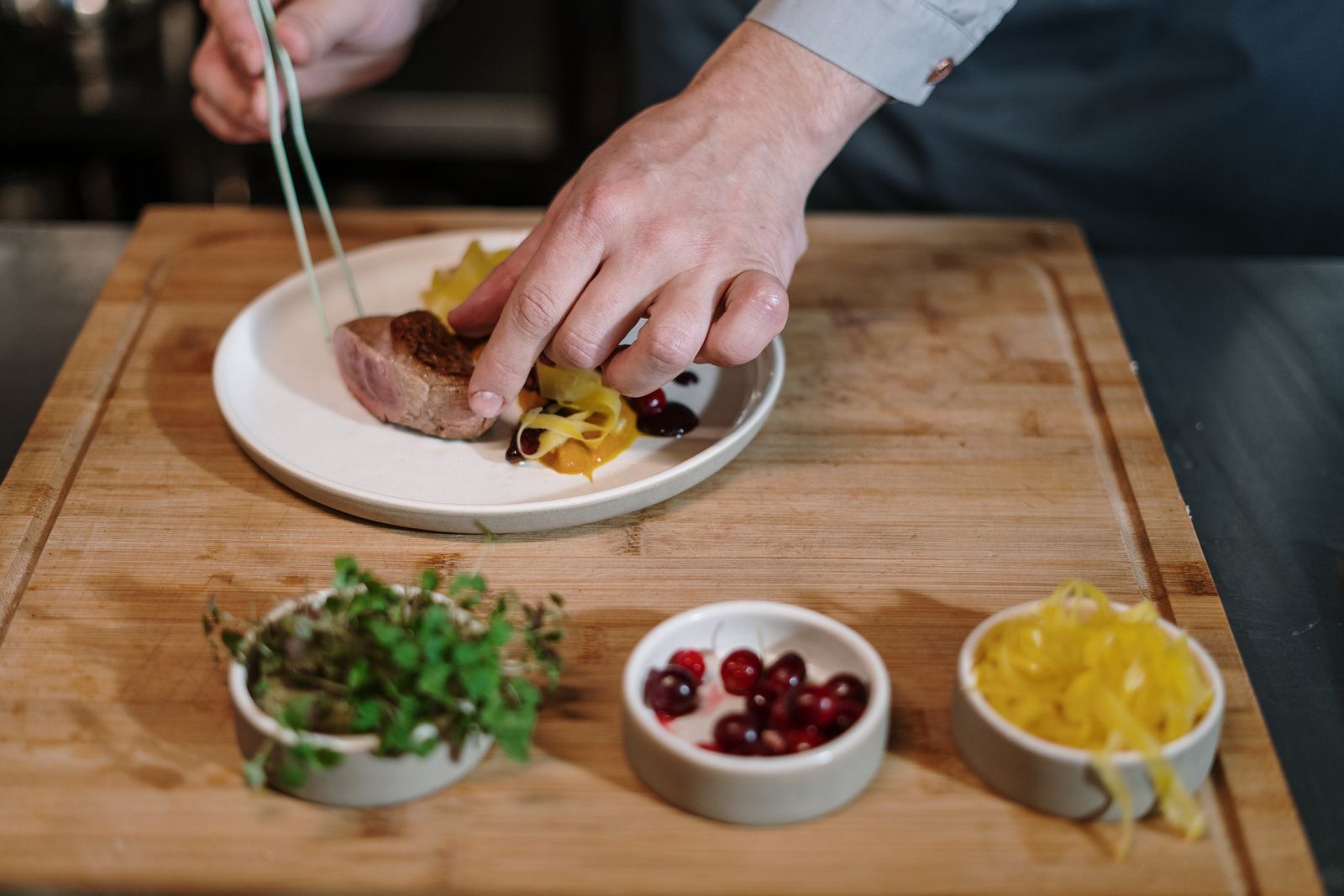 Two cooks plating a course with tweezers on a wooden board