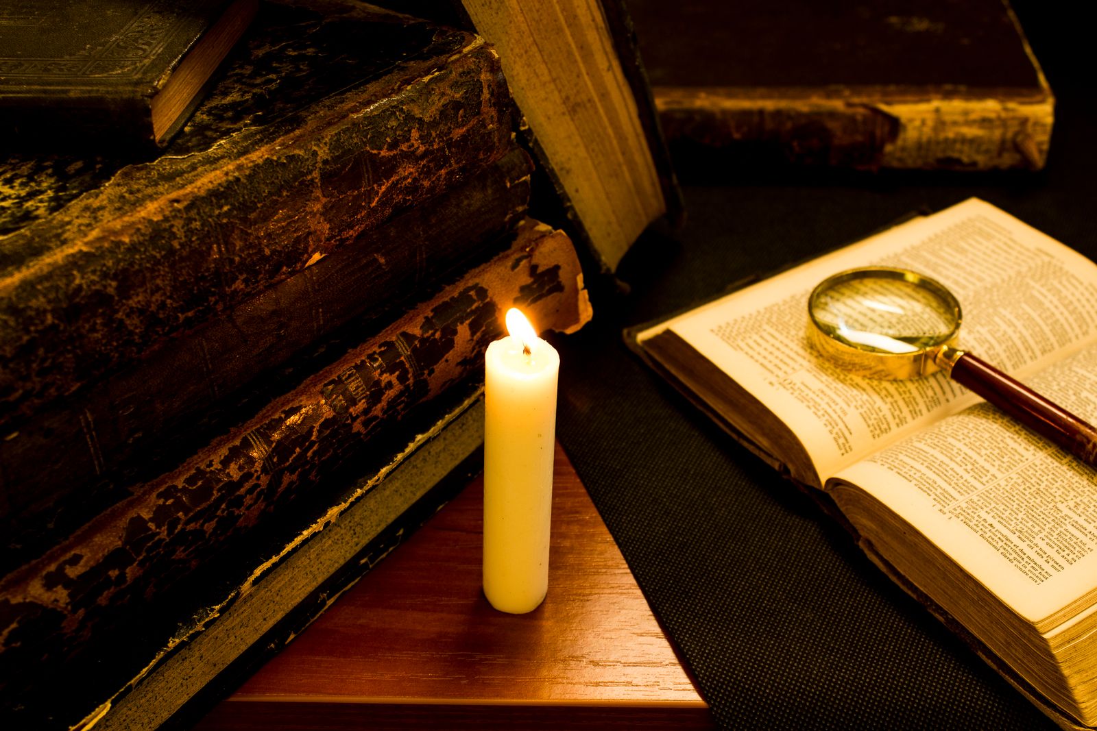 Candle burning beside old books and a brass magnifier