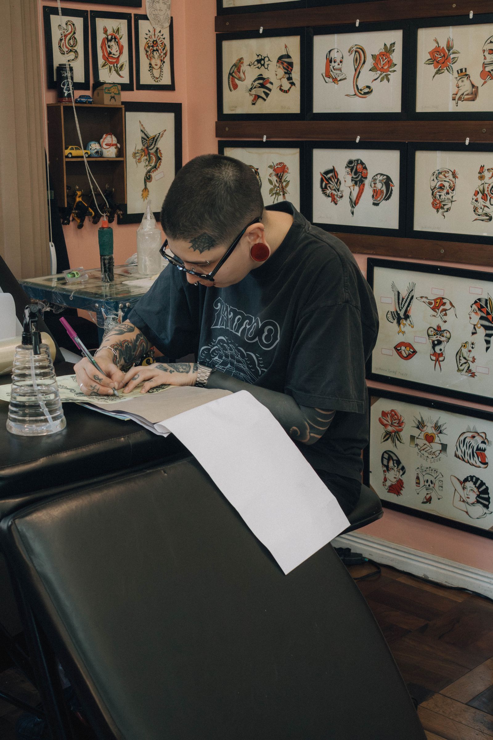 Artist drawing a custom design at a desk surrounded by flash sheets